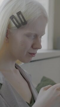 Carefree albino woman using smartphone messaging in social media relaxing in bed in apartment in morning. Gadget and modern lifestyle concept.