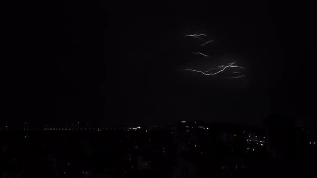 Dramatic lightning flashing across the dark night sky over a city skyline during a powerful thunderstorm