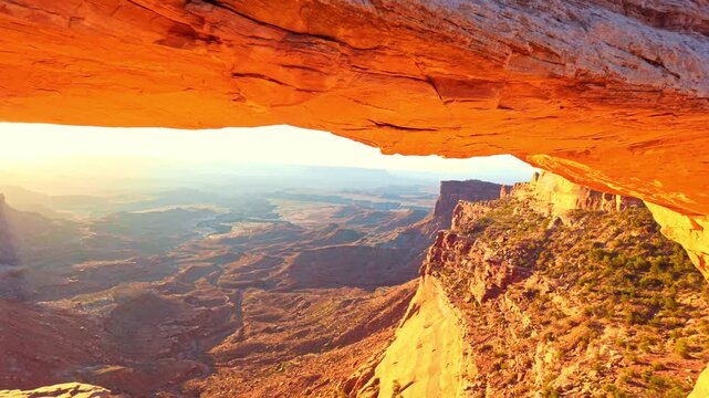 Early morning sunlight reflects intense fiery orange tones beneath Mesa Arch overlooking vast desert canyons in Utah
