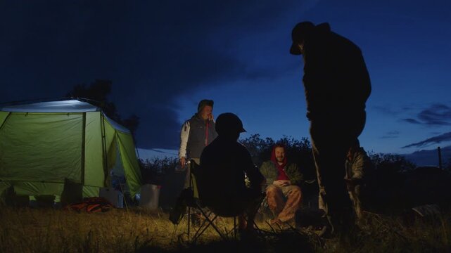 Group of men camping in the wild and gather near the bonfire and talk with each other. Fishermen camping and talk stories at night