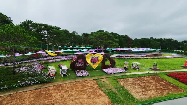 Aerial pan view of flower gardens with colorful umbrellas in park setting