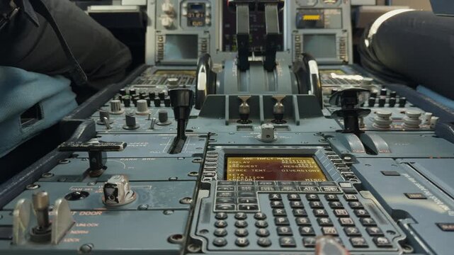 Close-up view of the centre pedestal, thrust levers and flight-management controls inside an Airbus A330 cockpit with two pilots seated.