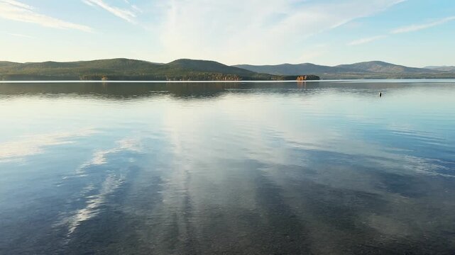 Autumn mountains and sky with clouds are reflected in the water. Beautiful autumn landscape. Turgoyak lake in Southern Urals, Russia.
