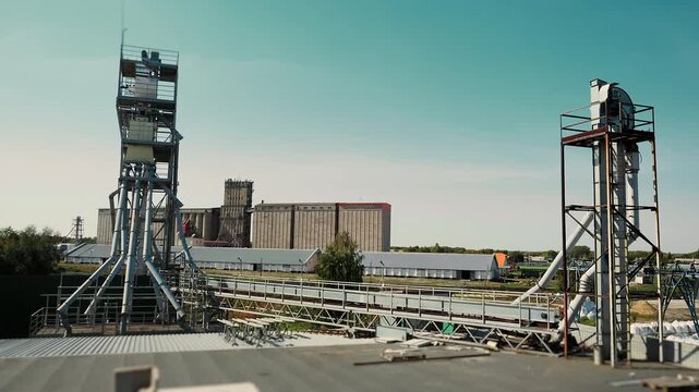Wide view of grain elevator equipment, conveyor systems and storage silos at an agricultural processing facility for grain handling and storage.
