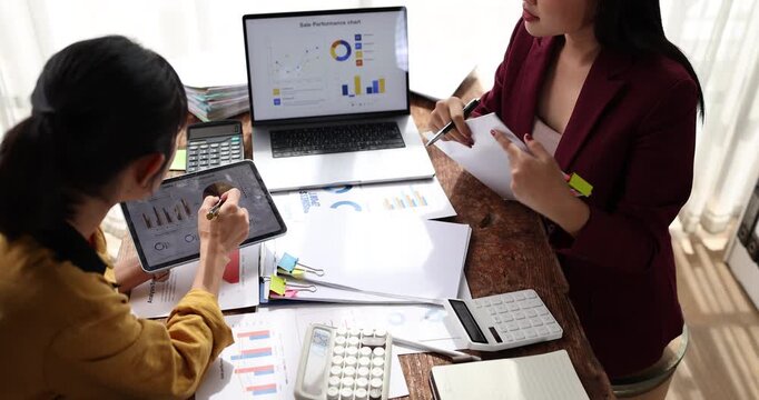 Businesswomen collaborating on financial data, analyzing reports and charts, planning investment strategies while working together in a professional office environment