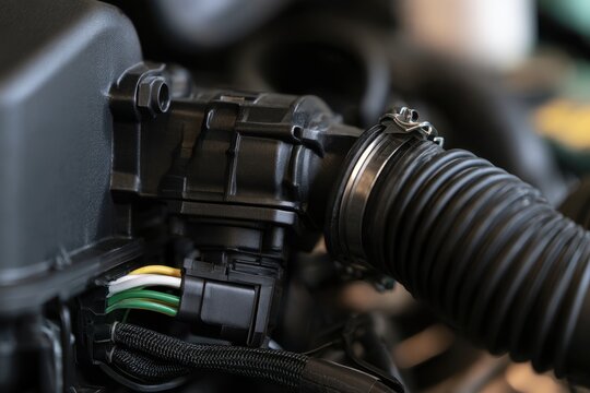 A close-up shot of an automobile engine bay showing a mass airflow sensor connected to an intake hose under soft workshop lighting.