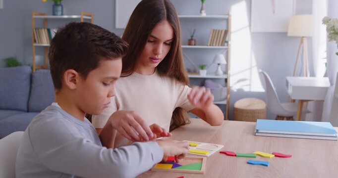 Two cheerful children sitting at wooden table and playing developing educational game together. Smiling brother and sister stacking colorful jigsaw pieces, collaborating to solve puzzles at home.