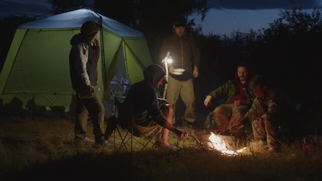 Group of men camping in the wild and gather near the bonfire and talk with each other. Fishermen camping and talk stories at night