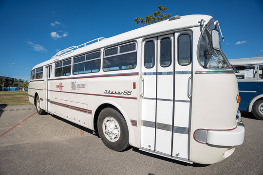 Vintage white Ikarus 66 bus parked outdoors on asphalt under a clear blue sky, classic retro coach vehicle with chrome trim