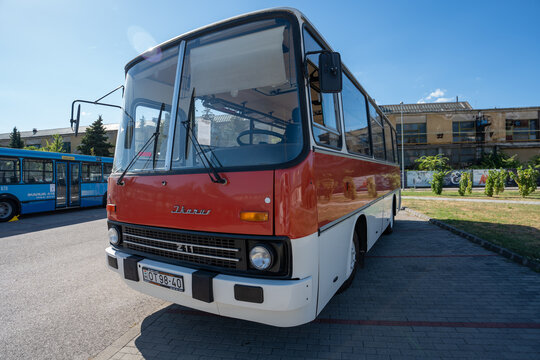 Vintage red and white retro coach bus parked outdoors on sunny asphalt lot, classic oldtimer transport vehicle with windshield