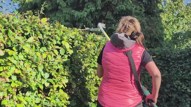 Woman trims bushes with electric trimmer featuring an adjustable angle head in a garden setting
