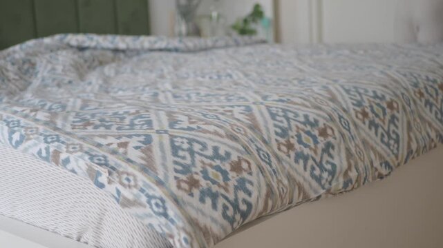 Woman smoothing patterned duvet cover on white bed during morning routine in bright bedroom.