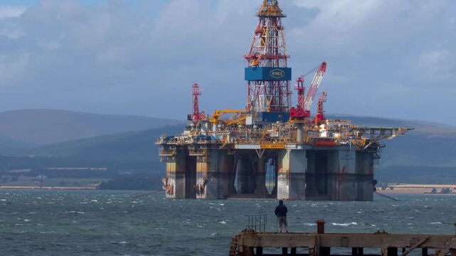 Offshore oil rig platform floating on choppy ocean water with land in background cinematic footage.