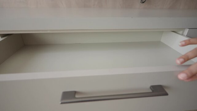 A woman pulls open a drawer in a grey kitchen cabinet made of modern materials