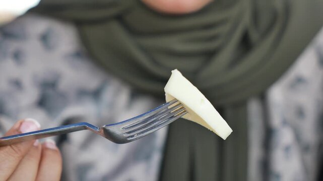 Person holds piece of cheese with a fork in hand at an outdoor setting