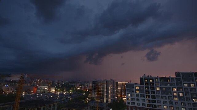 Lightning flashes over the buildings in a city. Rain and thunder storm over the city.