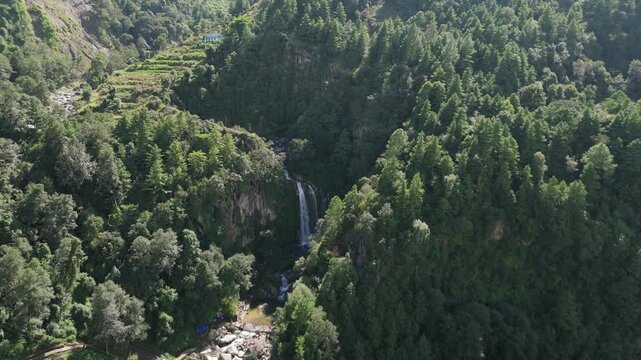 Wide aerial landscape of a plunging waterfall in a deep green mountain gorge bordered by terraced farms