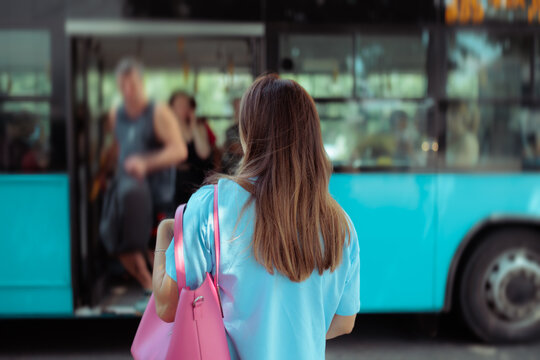 Woman With A Pink Bag Waiting To Board A Blue City Bus. Lady carries a pink trendy bag while waiting for a public bus
