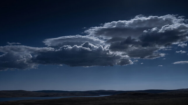 Dramatic moonlit clouds over a serene dark landscape with rolling hills and a distant lake at night