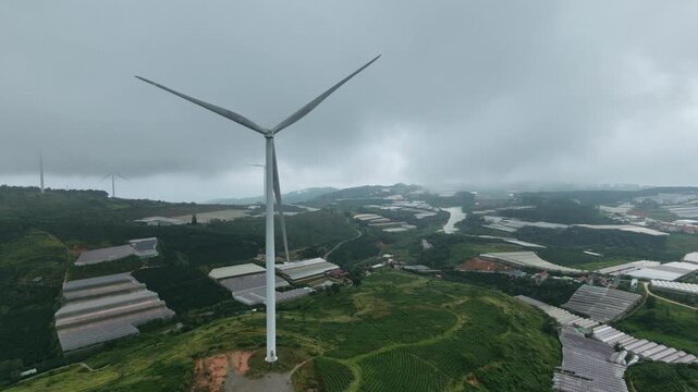 Aerial view of wind turbine spinning over green  Tea Hill agricultural landscape with cloudy sky, Cau Dat, Da Lat, Vietnam 