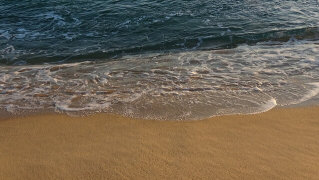 Peaceful early morning scenery of small ocean waves breaking onto the golden sand in Gangneung, South Korea.