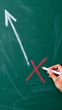 Hand drawing red X mark on green chalkboard, representing incorrect choice, error, denial, or wrong direction
