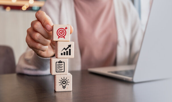Woman hand stacking wooden blocks with business icons, goal setting, strategy growth and planning step evaluation concept