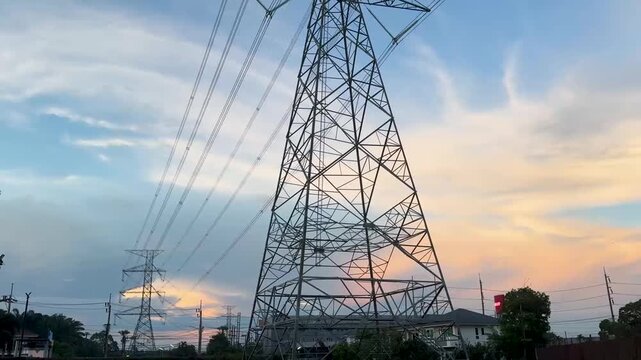High-voltage transmission towers and overhead power lines against a colorful sunset sky. Steel lattice pylons and electrical grid infrastructure in the evening light.
