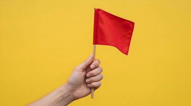 A human hand holding a small red flag isolated against a bright yellow background.