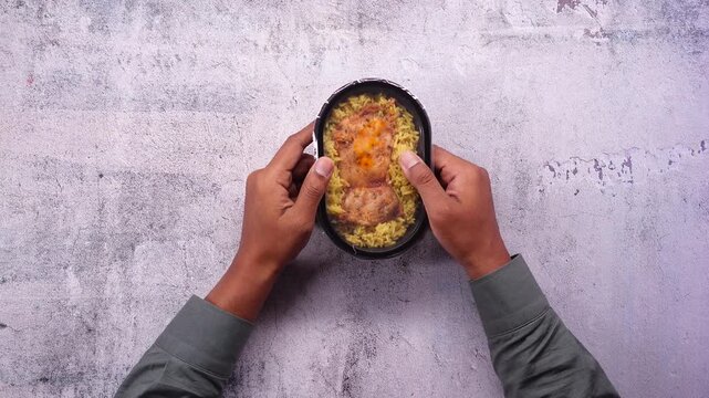Man hands holding a frozen microwaveable meal box with rice and chicken on a table.