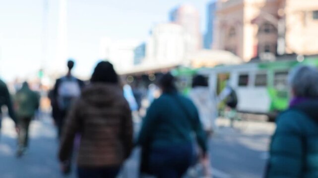 Blurred motion footage of busy pedestrian street with trams and buildings in background on sunny day.