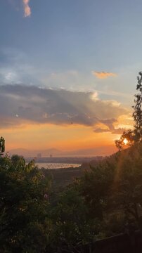 A scenic sunset over a river, with vibrant orange and blue hues in the sky. Silhouettes of trees frame the foreground, creating a tranquil atmosphere.