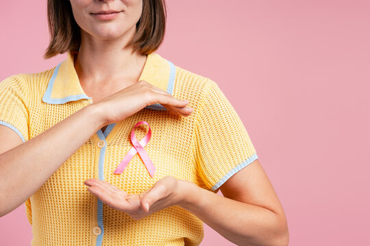 Woman protecting pink ribbon for breast cancer awareness selective focus, closeup