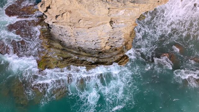 Waves hit the rocky shoreline in a coastal area. The water moves quickly, creating foam along the edges. This happens in broad daylight with clear visibility.