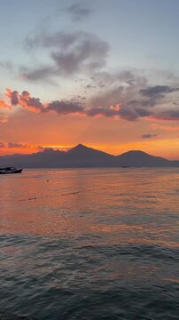 A serene sunset over calm waters with mountains in the background. The sky is filled with vibrant orange and purple hues, reflecting on the water's surface.