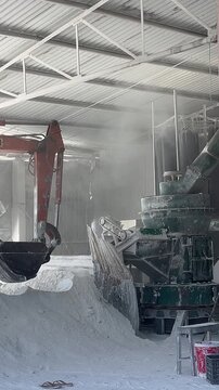 Industrial scene showing a large grinding machine in a factory. Dust and powder are visible on the floor, creating a busy manufacturing environment.