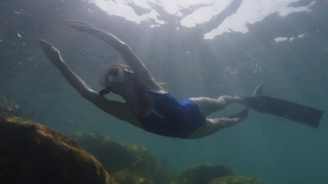 Young slim woman swims underwater, freediving and snorkeling in the sea near the coral reef near the island of Ilha Grande in Brazil