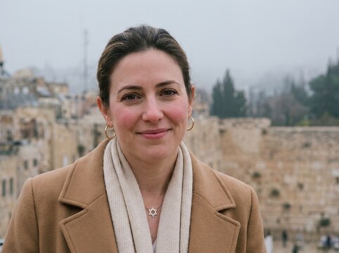 Portrait of smiling Jewish woman wearing Star of David necklace and warm winter coat outdoors in historic Jerusalem Old City, representing faith, heritage, and tradition
