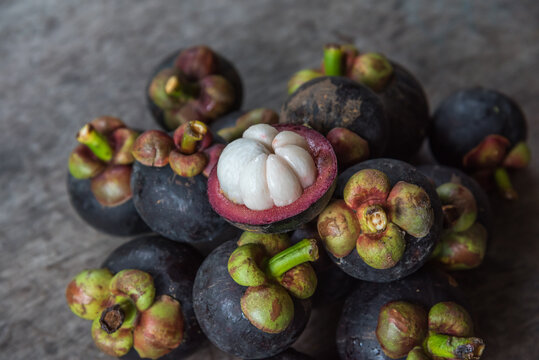 Fresh ripe mangosteen fruits one cut open revealing juicy white flesh surrounded by deep purple rind green calyx rustic wooden surface
