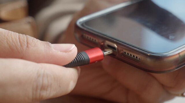 Close up shot of person plugging charging cable into smartphone port.