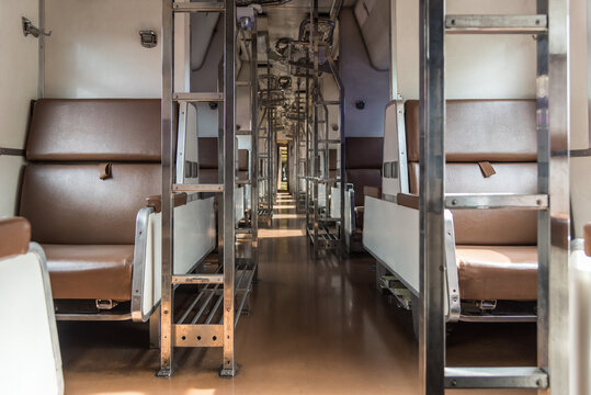 Empty passenger train carriage rows of brown seats metal luggage racks long central aisle creating quiet public transportation travel setting