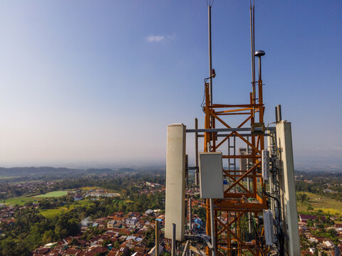 Multiple Radio Masts and Antenna Equipment on a Large Telecommunication Tower in a Rural Hilly Area Near a Populated Area in Indonesia. Communication Technology Viewed from Above.