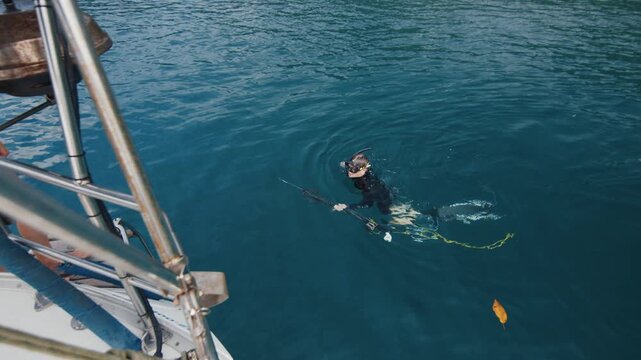 Man swims in the water with speargun towards the boat