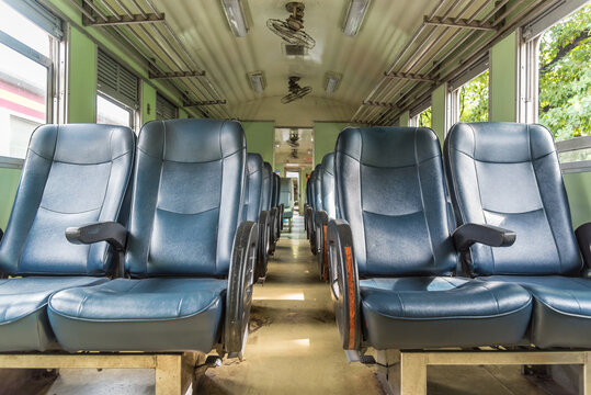 Empty passenger train interior rows of blue seats central aisle overhead luggage racks large windows representing railway travel public transit quiet journeys