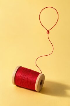 Red thread spool with loose string shaped like a balloon on a warm yellow background, symbolizing connection, creativity, aspiration and possibility. Concept of dreams, hope and imagination