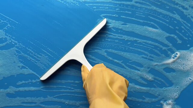 Removing Foam from a Blue Surface with a Squeegee in Closeup