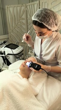 Cosmetologist performs ultrasonic facial cleansing on a teenage girl in a beauty salon, professional skincare, exfoliation, pore purification and gentle care.