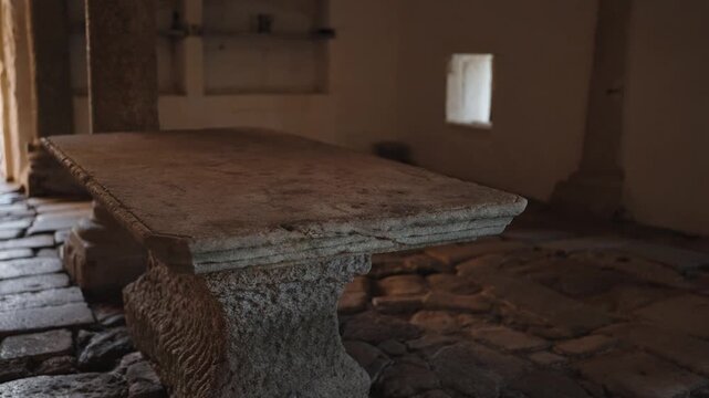 Heavy carved granite table stands on a cobbled floor in an empty whitewashed room of an old stone building.