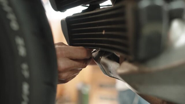mechanic uses a wrench on a motorcycle engine and exhaust header during a service and repair job in a vehicle workshop with the front tire visible in the frame