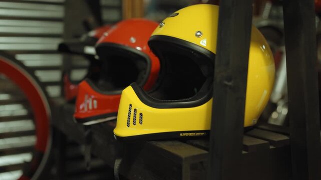 Yellow and red full face helmets with dark visors rest on a wooden shelf inside a motorcycle repair workshop.